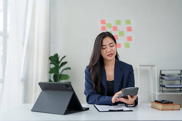 Young asian businesswoman working diligently on a financial report while using a calculator in a modern office environment