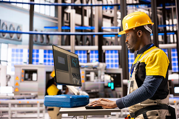 Black male technician manages autonomous manufacturing system, overseeing robotic arms and conveyor belts for improved industrial efficiency. Industry 4.0 specialist handles smart factory optimization
